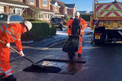 Two men in hi-vis are pouring in and raking asphalt in a pothole repair